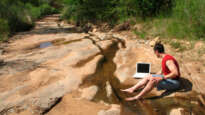 Man on laptop by desert stream